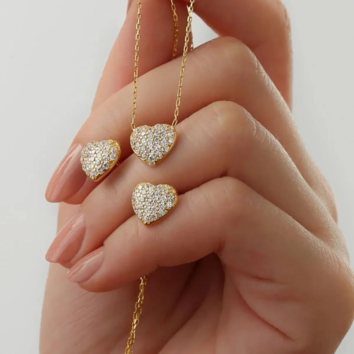 Minimal taşlı kalp kolye-küpe set, elde yakın görünümü.