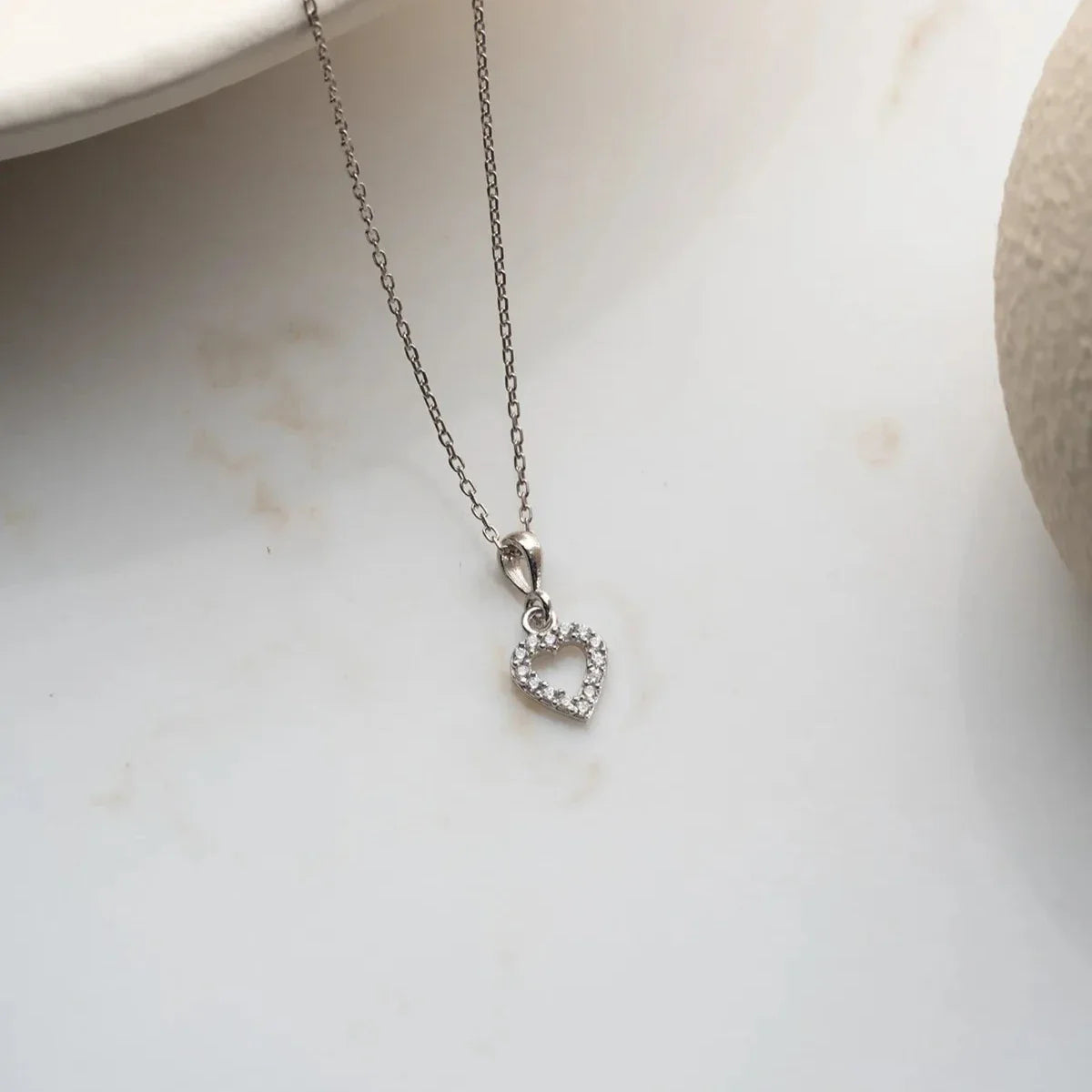 Zirkon taşlı mini love kolye, zemin üzerinde görünümü.