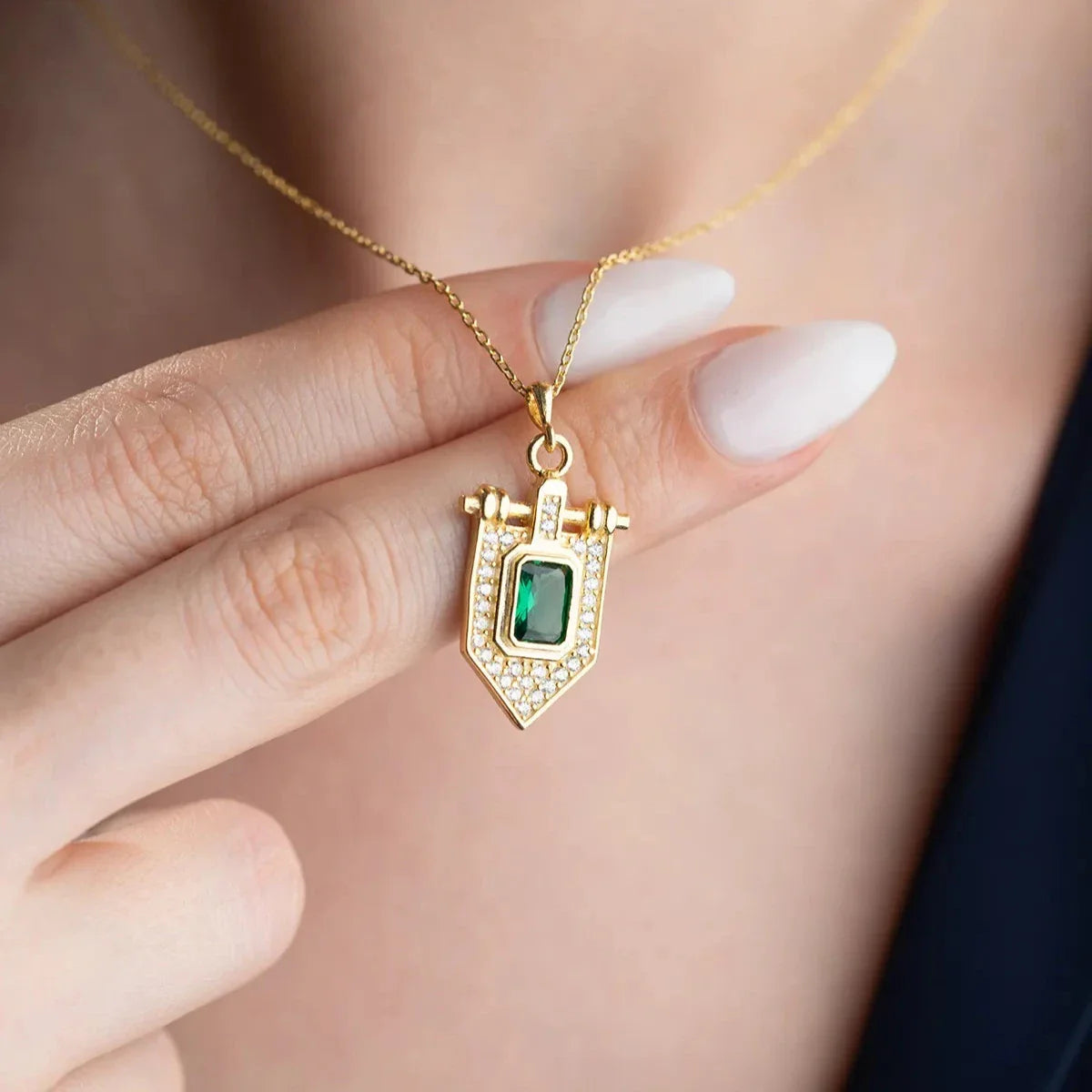 Zümrüt taşlı üçgen kolye, elde yakın görünümü.