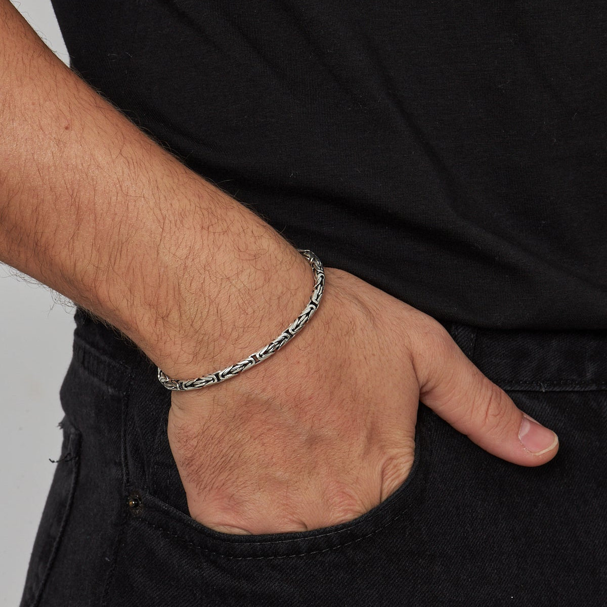 Gümüş renkli 4 mm yuvarlak kral zincir erkek bilekliği, eli cebinde duran modelin bileğinde.