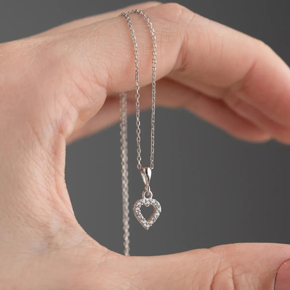 Zirkon taşlı mini love kolye, elde yakın görünümü.